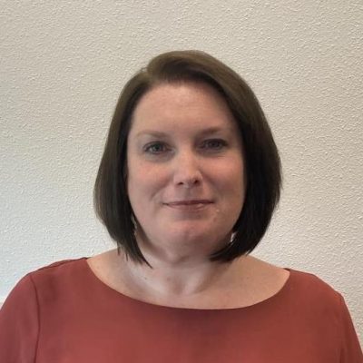 Dr. Hope Schuermann, female with shoulder-length brown hair wearing a rust-colored top against a textured, off-white background.