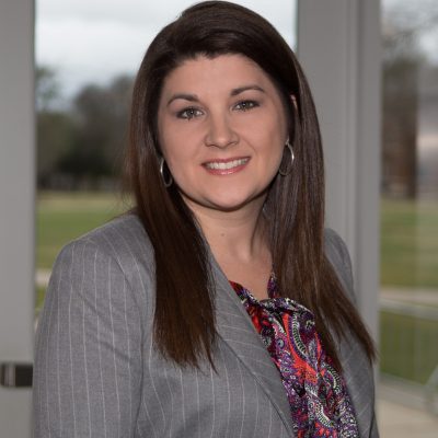 Dr Rochelle Cade, female with long brown hair and brown eyes wearing a gray stiped business suit. 