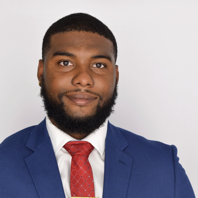 Dr. Jordan Mike. A man in a blue suit and red tie stands against a plain white background.